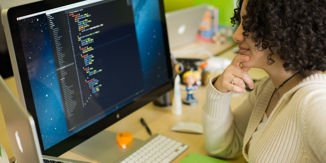 Woman coding CSS with a code editor and large screen.